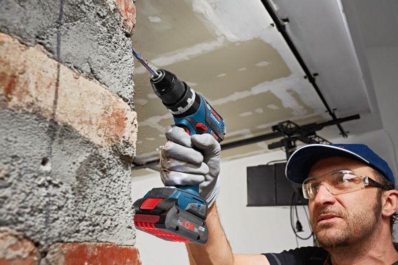 ProCORE18V 4.0Ah A person wearing safety equipment drills into a brick wall with a cordless power drill.