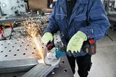 A person wearing safety equipment grinds metal with an angle grinder, producing sparks.