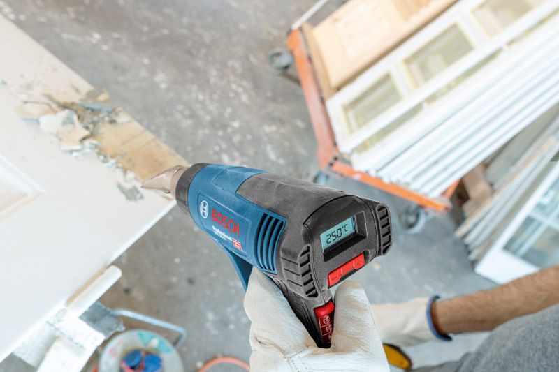 GHG 20-63 A person wearing safety equipment uses a heat gun to remove paint from a door.