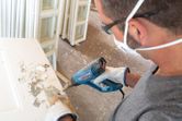 A person wearing safety equipment uses a heat gun to strip paint from a door.