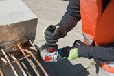 A person wearing safety equipment cuts rebar with an angle grinder, causing sparks.