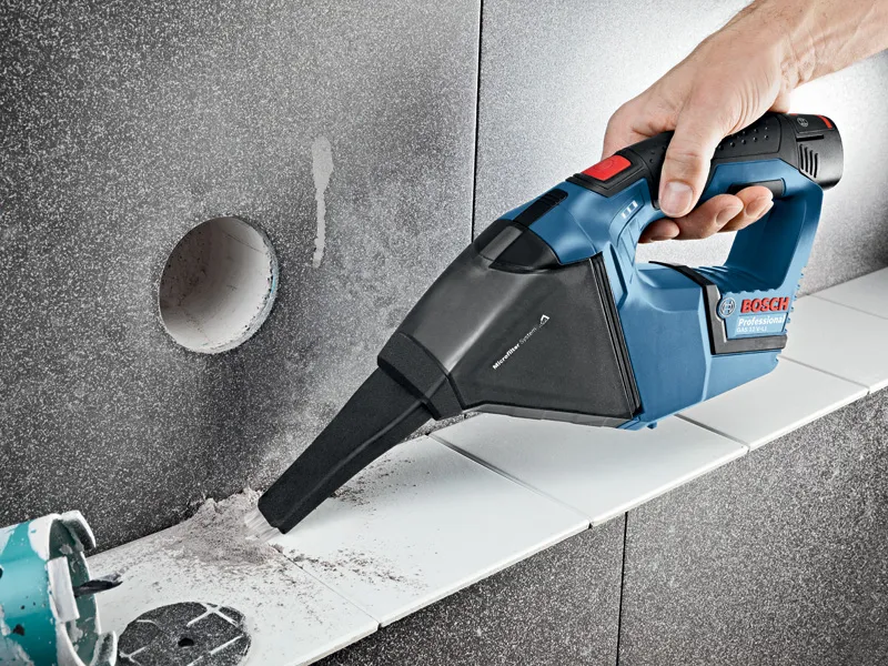 GAS 12 V-LI Person uses a cordless vacuum cleaner to remove dust from a tiled surface.