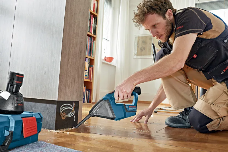 GAS 12 V-LI A person wearing safety equipment uses a cordless vacuum cleaner to clean wood shavings.