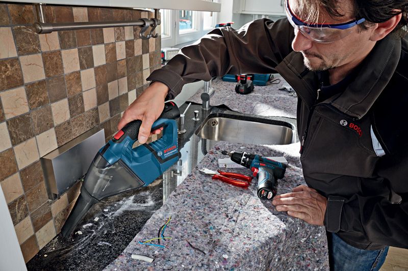 GAS 12 V-LI Person wearing safety equipment cleans construction debris with a cordless vacuum cleaner.