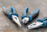 Three-piece plier set with blue and black handles arranged on a metal surface.