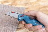 Person holds a utility knife, preparing to cut a piece of carpet.