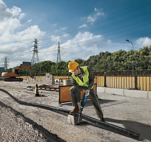 GSA 120 A person wearing safety equipment uses a reciprocating saw to cut a pipe at a construction site.