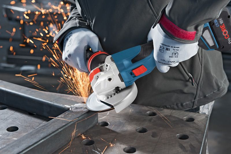 A person wearing safety equipment grinds metal with a cordless angle grinder.