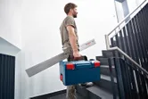 A person carries a tool case and an angle measurer while walking up stairs.