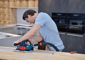 A person wearing safety equipment cuts wood using a circular saw with dust extraction.