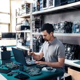 A person uses a cordless screwdriver to assemble electronic components at a workbench.