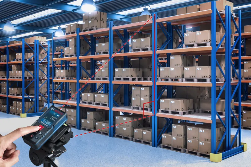 A person uses a laser measure to check distances between warehouse shelves.