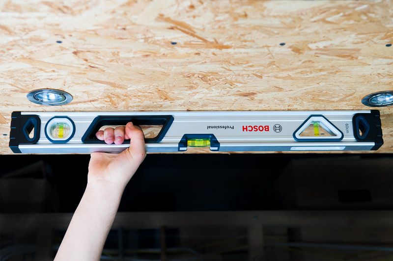 Level 60 cm A person holds an optical level against a wooden ceiling for alignment.