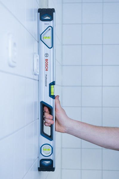 Level 60 cm Person holding a 60cm optical level upright against a tiled wall.