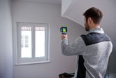 A person scans a window area with a thermo camera inside a building.