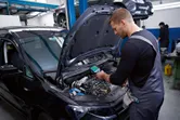 A person wearing safety equipment inspects a car engine with a thermo camera.