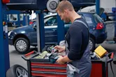 A person wearing safety equipment checks a thermo camera at a tool cart in an auto workshop.