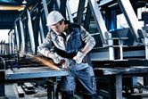 A person wearing safety equipment grinds metal beams with a cordless angle grinder.