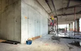 A person wearing safety equipment uses a laser leveling tool on a concrete wall.