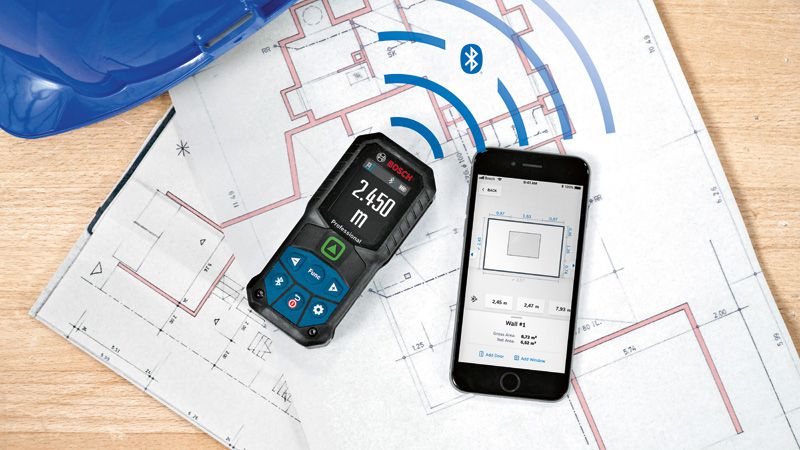 Laser measure and smartphone displaying measurements, placed on architectural blueprints.