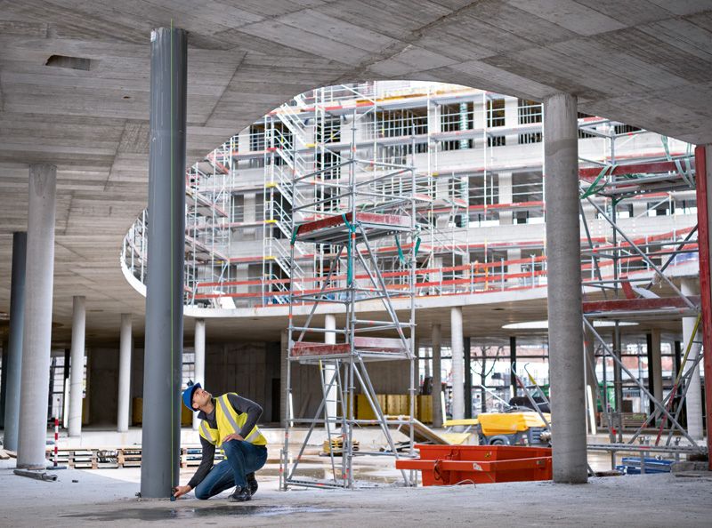 GLM 50-27 CG A person wearing safety equipment uses a laser measure on a column at a construction site.