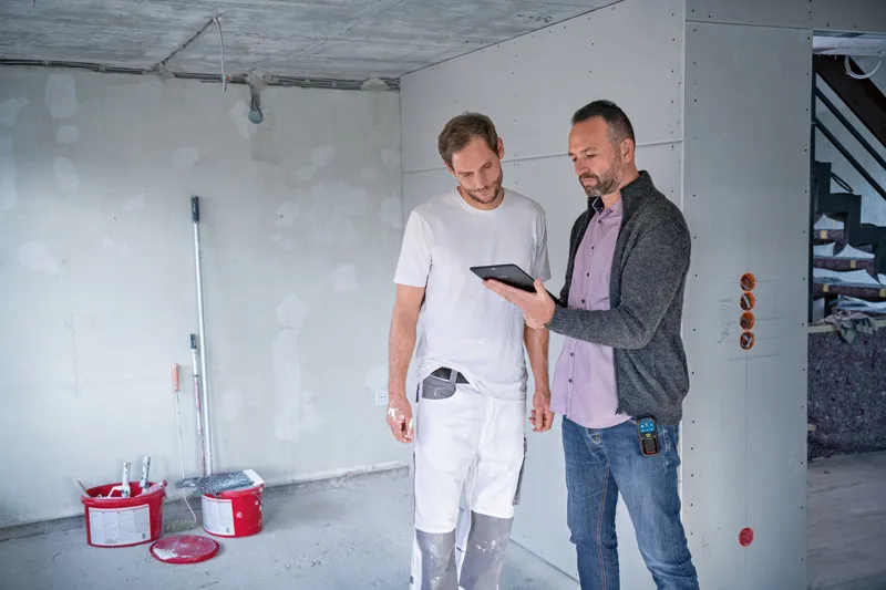 GLM 50-27 CG Two people review construction plans on a tablet, one holds a digital measuring device.