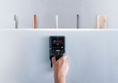 A person scans a drywall with a detector, identifying hidden pipes and wires.