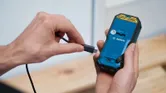 A person connects a charging cable to the back of a handheld power tool.
