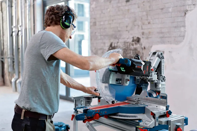 GCM 18V-305 GDC A person wearing safety equipment operates a cordless mitre saw on a workbench.