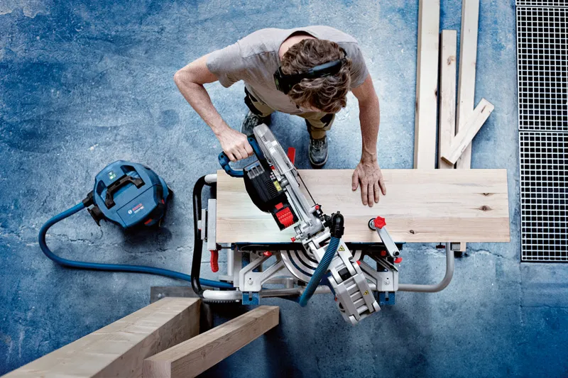 GCM 18V-305 GDC A person wearing safety equipment cuts a wooden plank with a cordless mitre saw.