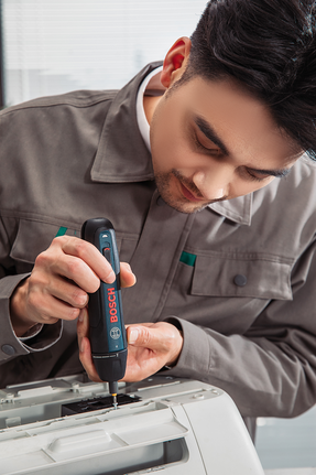 Person assembling an office machine with a cordless screwdriver.