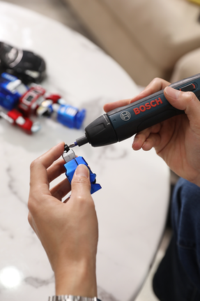 Person using a cordless rotary tool to polish a small blue plastic object.