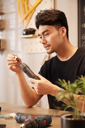 Person inserting a drill bit into a cordless screwdriver at a workbench.