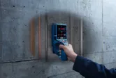 Person scanning a concrete wall with a digital detector, revealing pipes and wiring inside.
