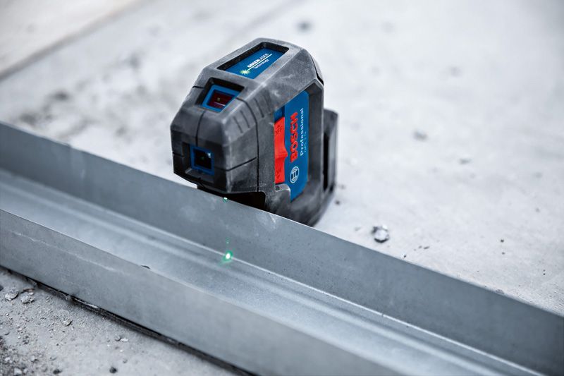Laser leveling tool projecting green lines onto a metal track on a concrete floor.