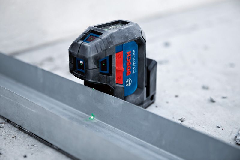 Laser leveling tool projecting green points onto a metal track on a concrete floor.