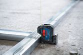 Laser leveling tool projecting green lines onto metal tracks at a construction site.