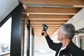 A person scans a wooden ceiling with a thermo detector in a bright room.