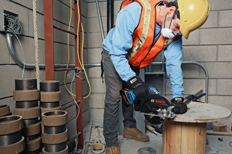 A person wearing safety equipment cuts wood with a handheld saw on a construction site.