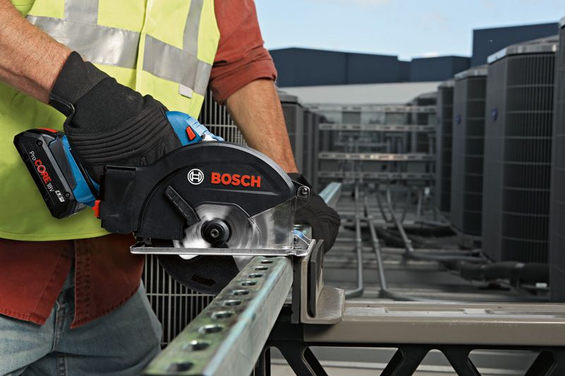 A person wearing safety equipment cuts a metal beam with a cordless circular saw.