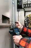 A person uses a thermo detector to check wiring inside an electrical cabinet.
