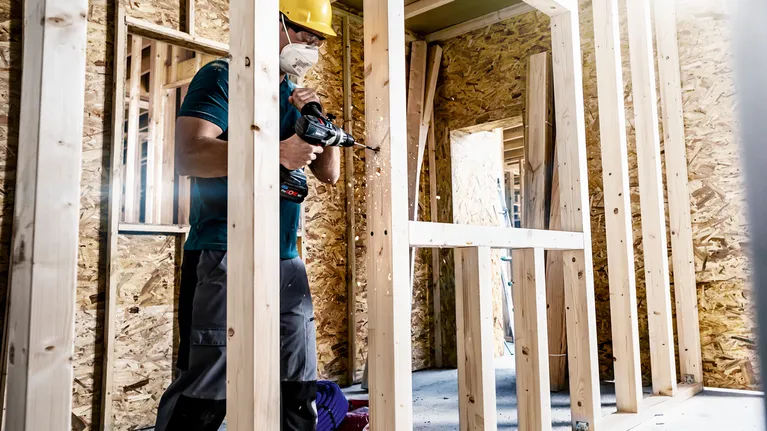 EXPERT Self Cut Speed Spade Drill Bit Set 13/16/19/20/22/25 mm 6-pc A person wearing safety equipment drills into a wooden frame at a construction site.