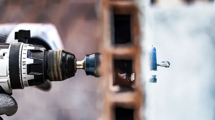 A person wearing safety equipment drills into a brick wall using a power tool.