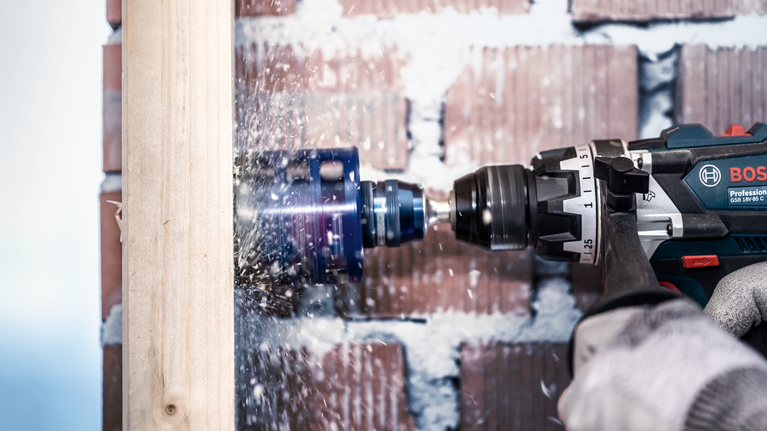 EXPERT Power Change Plus Hole Saw System Arbor 11 mm, TCT Drill 8.5 x 105 mm, 2-pc Person wearing safety equipment drills a large hole in a wooden beam.