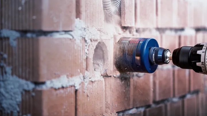 Rotary tool drilling a circular hole in a brick wall.