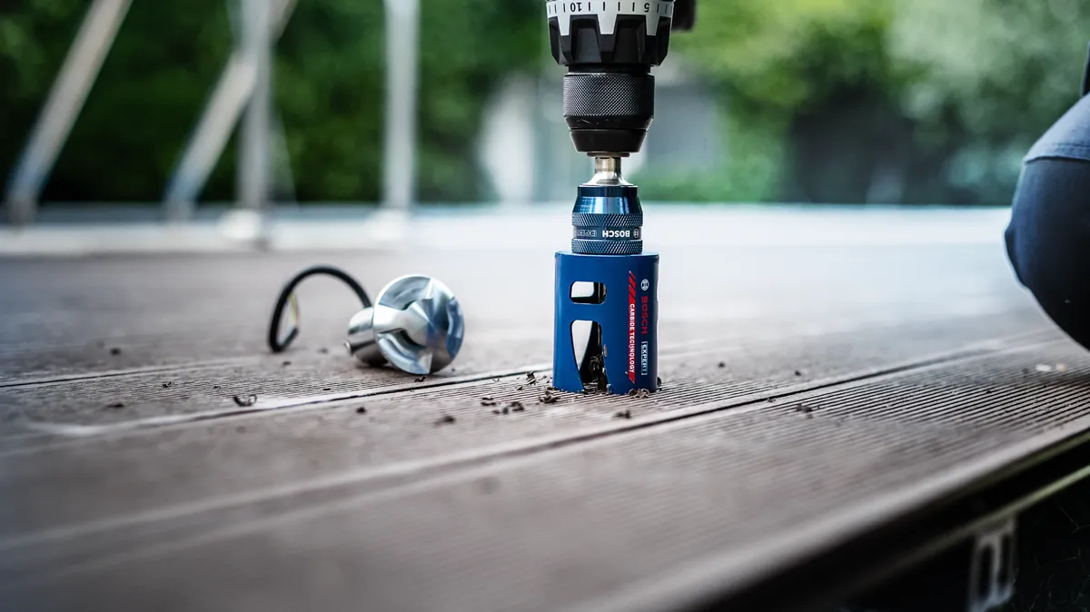 Hole saw drill bit cutting a hole in a wooden deck plank.