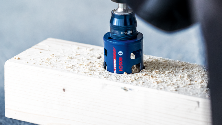 EXPERT Construction Material Hole Saw 68 x 60 mm Hole saw drilling a circular opening in a wooden plank.