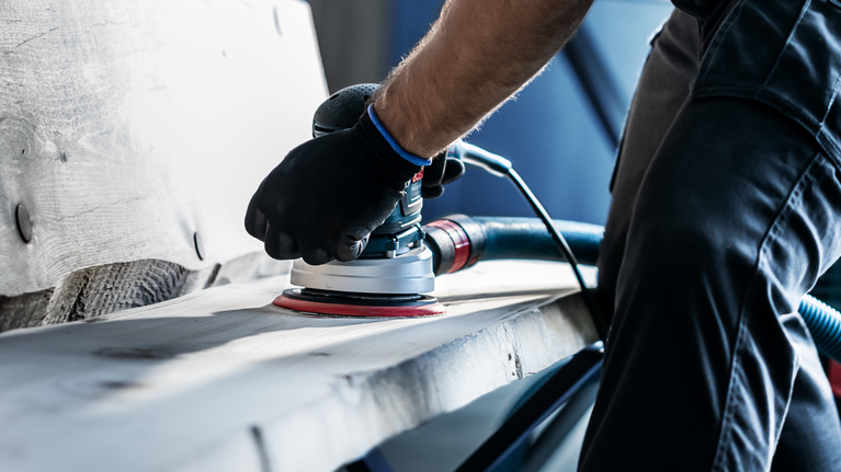 EXPERT M480 Sanding Net for Random Orbital Sanders 125 mm, G 80 5-pc Person wearing safety equipment sanding a wooden surface with a power sander.