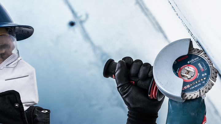 Person wearing safety equipment uses an angle grinder to cut a metal surface.