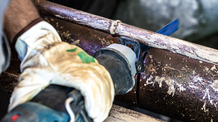 EXPERT ‘Thick Tough Metal’ S 955 CHC Reciprocating Saw Blade 1-pc A person wearing safety equipment cuts a rusted metal pipe with a reciprocating saw.